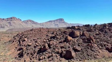 Açık mavi gökyüzünün altındaki çarpıcı ve engebeli kayalık arazileri keşfedin, doğal jeolojik güzellikleri sergileyin.
