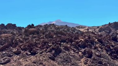Berrak mavi gökyüzünün altındaki volkanik kayaların nefes kesici manzarası engebeli arazileri ve uzak tepeleri gösteriyor..