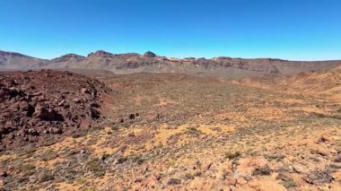 Göz kamaştırıcı bir panoramik manzara berrak mavi gökyüzünün altında uzanan nefes kesici kayalık bir çöl manzarası sergiliyor.
