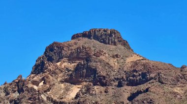 Sersemletici bir kayalık dağ zirvesi açık mavi bir gökyüzü altında yükselir, doğa meraklıları ve açık hava aşıkları için idealdir.