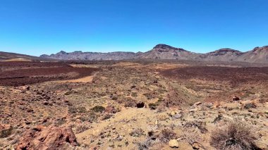 Issız ve çorak çöl arazisinin nefes kesici manzarası, etrafındaki canlı renklerle kayalık tepeleri sergiliyor.