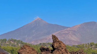 Kayalık arazi ve canlı yeşil yeşilliklerle çevrelenmiş aktif bir volkanın çarpıcı manzarası.