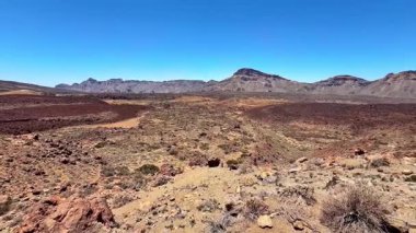 Issız ve çorak çöl arazisinin nefes kesici manzarası, etrafındaki canlı renklerle kayalık tepeleri sergiliyor.
