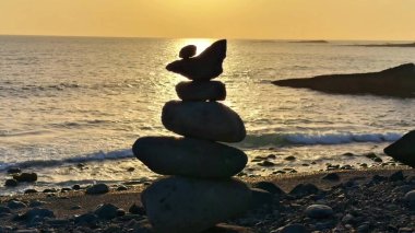 Güzelce dingin bir sahil sahnesi dikkatlice dengelenmiş taşları sergiliyor nefes kesici bir günbatımı arka planına karşı.