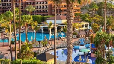 Palmiye ağaçları ve tatil günü için ideal su kaydırağıyla lüks bir otel havuzu manzarasının tadını çıkarın.