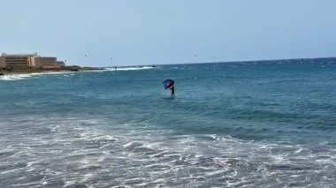 Göz kamaştırıcı bir uçurtma sörfçüsü berrak mavi gökyüzü ve güneşin altındaki güçlü dalgaları ustalıkla okyanuslarda yüzüyor.