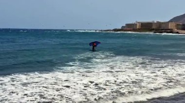 Okyanus dalgalarına karşı canlı bir şemsiyeyle suda dengede duran bir insanın heyecanlı anı..