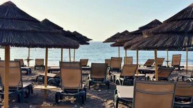 Huzurlu, sakin denizi gören rahatlatıcı bir plaj sahnesi şezlonglar ve renkli şemsiyeler.