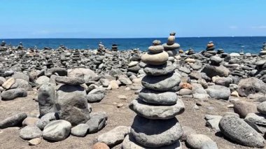 Huzurlu ve sakin bir sahil sahnesi. Okyanus dalgaları yakınında dikkatlice dengelenmiş taş yığınları.