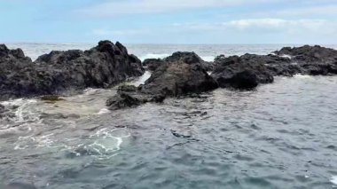 Parlak mavi gökyüzünün altında berrak okyanus sularından yükselen kayalık oluşumların şaşırtıcı derecede sakin bir görüntüsü.