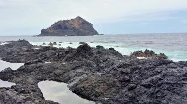 Çarpıcı kayalık kıyı şeridi ufukta uzak bir adayla kıyıya vuran dalgalara sahiptir.