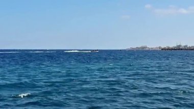 Açık mavi bir gökyüzünün altında turkuaz sularda yüzen bir sürat teknesiyle pitoresk bir okyanus sahnesi.