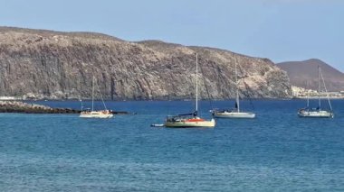 Sakin ve huzurlu bir manzarayla sakin sularda demirlemiş güzel yelkenliler, çarpıcı bir kayalık zemin.