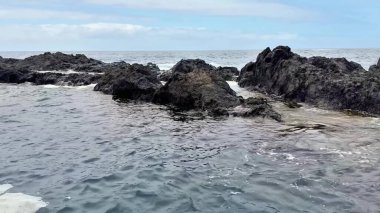 Etkileyici kayalık oluşumların, berrak, parlak mavi gökyüzünün altında hafif dalgalarla nefes kesici bir görüntüsü.