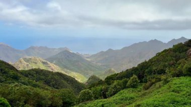 Bulutlu bir gökyüzünün altındaki yeşilliklerle çevrili, doğa meraklıları için mükemmel bir dağ manzarası..