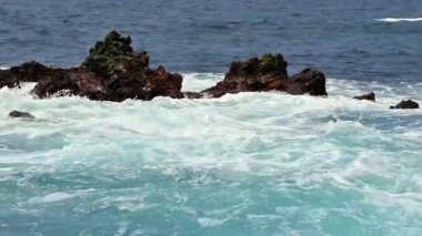 Güçlü okyanus dalgaları güçlü bir şekilde pürüzlü kayalara çarpar, doğanın gücünü ve eşsiz güzelliğini gösterir.