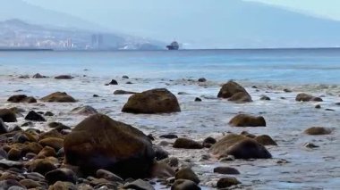 Huzurlu ve rüya gibi bir gökyüzünün altında sakin okyanus suyunun yanında engebeli kayalar sergilenen güzel bir kıyı manzarası.