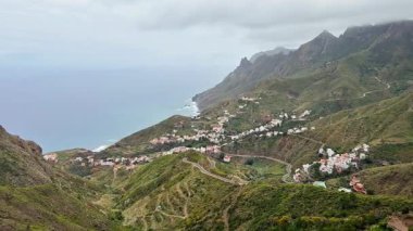 Dramatik gökyüzünün altında yemyeşil dağlara kurulmuş büyüleyici bir sahil kasabasının nefes kesici panoramik manzarası.
