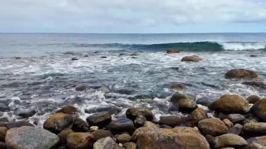 İnanılmaz bir manzara ve sakin dalgalar bulutlu gökyüzünün altında kayalık bir sahile yavaşça çarpıyor.