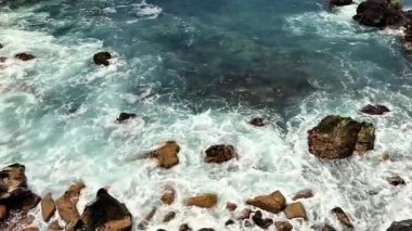 Bu sakin sahil sahnesinde dalgaların engebeli kayalara çarptığı büyüleyici bir hava manzarası yaşayın.