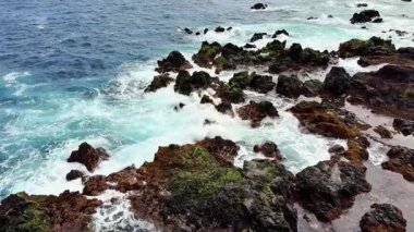 Dalgaların kıyıya çarptığı kayalık bir kıyı şeridinin çarpıcı hava manzarası canlı bir deniz manzarası yaratıyor.