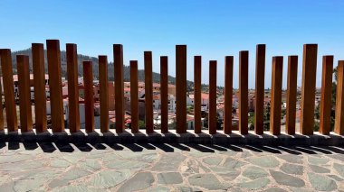 Uzun, ahşap bir çit, parlak mavi bir gökyüzüne ve nefes kesici bir manzaraya karşı karmaşık gölgeler bırakır.