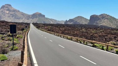 Göz kamaştırıcı bir yol, berrak gökyüzünün altındaki görkemli dağlarla çevrili eşsiz bir volkanik arazide esiyor.