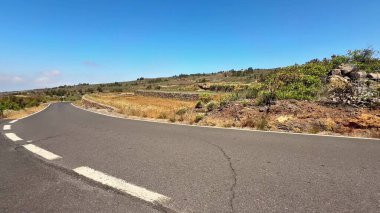 Güzel, dolambaçlı bir yol kuru otlaklarda ve kayalık arazide geziniyor, hepsi parlak mavi bir gökyüzünün altında.