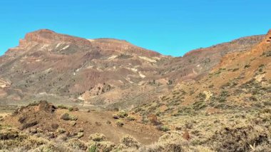 Berrak mavi gökyüzünün altında kurak manzarayla birleşen kayalık dağların nefes kesici ve çarpıcı manzarasını deneyimleyin.