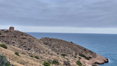 Kesinlikle nefes kesici bir manzara, sakin okyanusun yanındaki bir tepenin üzerinde heybetli bir şekilde duran tarihi bir kuleyi gözler önüne seriyor.