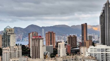 Bulutlu bir gökyüzü altında kıyı manzarası, dağlar ve şehir mimarisi barındıran nefes kesici bir şehir..