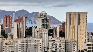 Modern bir kıyı şehrinin panoramik manzarası, şehir mimarisini gözler önüne seren, dağlık bir zemin üzerine kurulmuş..