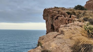Bulutlu ve dramatik bir gökyüzünün altında sakin ve sakin okyanusa bakan nefes kesici ve çarpıcı bir uçurum manzarası.