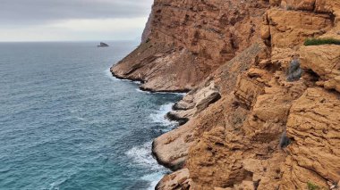 Gerçekten muhteşem bir kıyı manzarası engebeli uçurumları sergiliyor. Geniş gri gökyüzünün altındaki sakin suların yanında.