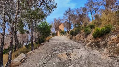 Resmedilmesi zor ve dolambaçlı bir patika güzel bir yamaçtan yükselir, yemyeşil ağaçların sardığı,
