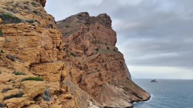 Göz kamaştırıcı ve güzel manzaralar bulutlu bir gökyüzünün altındaki engebeli kıyı şeridini çevreleyen kayalık uçurumları gösteriyor.