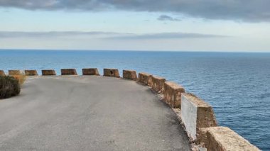 Huzurlu ve huzurlu bir sahil manzarası bulutlu bir gökyüzünün altında muhteşem okyanus manzaralı dolambaçlı bir yolu gösteriyor.