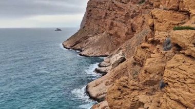 Gerçekten muhteşem bir kıyı manzarası engebeli uçurumları sergiliyor. Geniş gri gökyüzünün altındaki sakin suların yanında.
