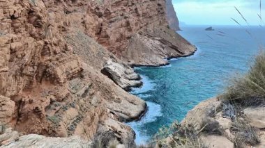 Kıyıdaki berrak mavi sularla görkemli bir şekilde buluşan kayalık kayalıkların nefes kesici ve çarpıcı manzarasına tanık olun.