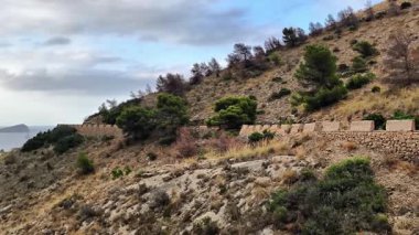 Bu video, dağları takip eden taştan bir duvarla çarpıcı bir yamaç manzarası, yemyeşil bir alan ve güzel manzaralar sunan dolambaçlı bir yol gösteriyor.