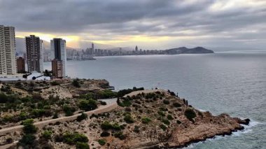 Okyanusun üzerindeki çarpıcı bir uçurumun havadan görünüşü, arka planda pitoresk bir şehir, kentsel yaşamla ahenk gösteriyor.