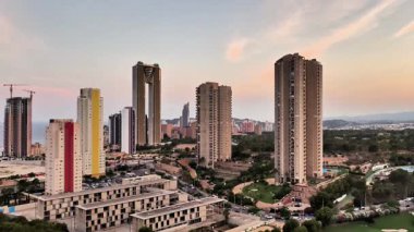 Yüksek binalarla dolu canlı bir şehir silueti, önplanda modernlik ve doğayı harmanlayan manikürlü bir golf sahası ile tezat oluşturuyor.