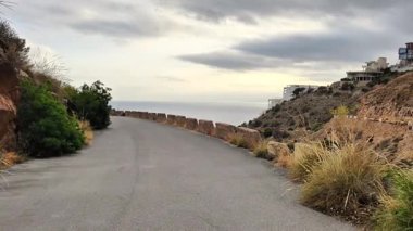 Video, bulutlu bir gökyüzünün altında nefes kesen okyanus manzarasını gözler önüne seren dolambaçlı bir yola sahip manzaralı bir sahil turu seriyor.