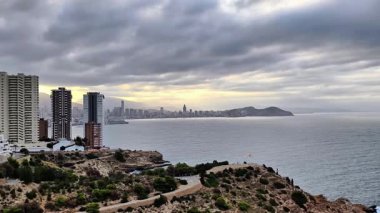 Çarpıcı okyanus manzaralı bir tepenin üzerindeki kıyı şehrini deneyin. Bu sinematik yolculuk havadan bakış açılarını ve sakin manzaraları vurguluyor, dalgalara karşı şehrin ufuk çizgisini gösteriyor.