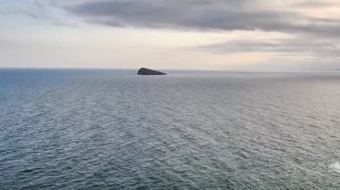 Bu video, bulutlu bir günde okyanusların güzelliğini sergiliyor, sakin sularla çevrili küçük bir adayı gözler önüne seriyor.