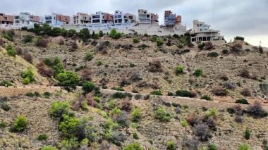 Bu video, doğa ve kentsel gelişimin karışımını vurgulayan, bir tepenin üzerindeki evlerin ve modern binaların resimsel manzarasını sergiliyor.