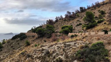 Bu video, dağları takip eden taştan bir duvarla çarpıcı bir yamaç manzarası, yemyeşil bir alan ve güzel manzaralar sunan dolambaçlı bir yol gösteriyor.