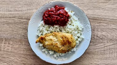 Güzel düzenlenmiş bir tabak pirinç ve ahududu aromalı ve kızılcık soslu yumuşak tavuk, sade ahşap bir masa üzerine kurulmuş.