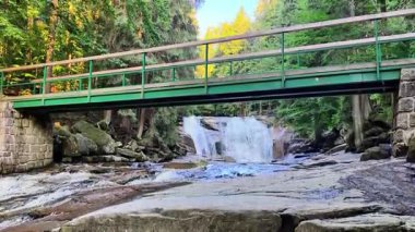 Güzelliği, sakin bir nehir, çarpıcı bir şelale ve sık bir orman, somut bir ahenk üzerine yemyeşil bir köprü görüntüsüyle tecrübe eder.