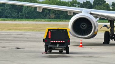 Küçük sarı ve siyah bir kamyon havaalanı pisti boyunca ustalıkla büyük bir uçağı çekiyor ve havacılık sektöründeki hayati lojistiği gösteriyor.